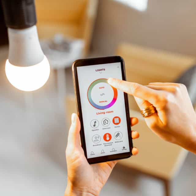 Person using a smartphone app to control a living room light. The interface shows brightness and on/off options.