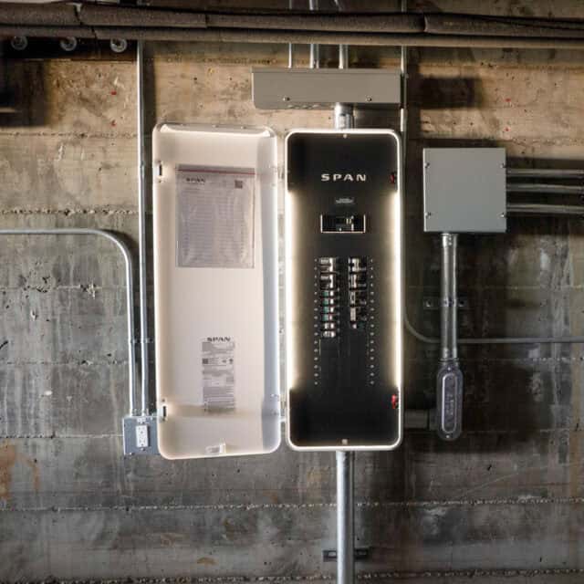 An open electrical panel attached to a wall with labeled switches and wiring visible.