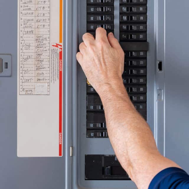 A person adjusts a breaker switch in an open electrical panel.