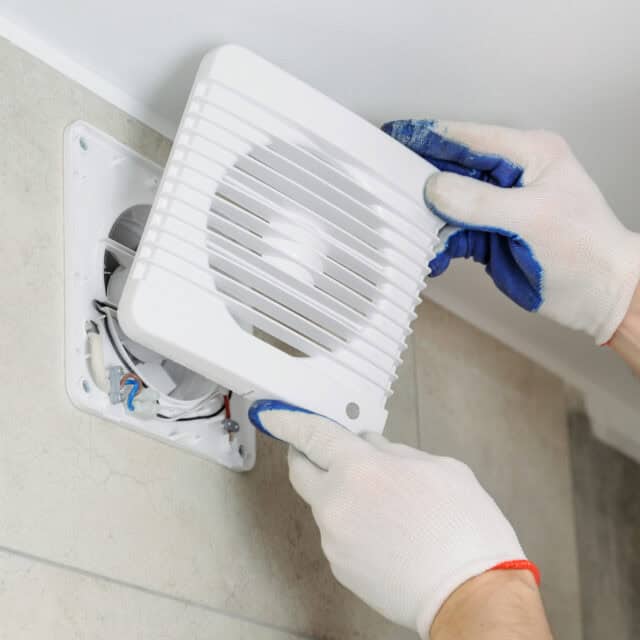 Person wearing gloves installs a white vent cover on a wall.