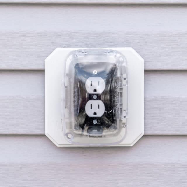 Outdoor electrical outlet with cover mounted on a vinyl siding wall.