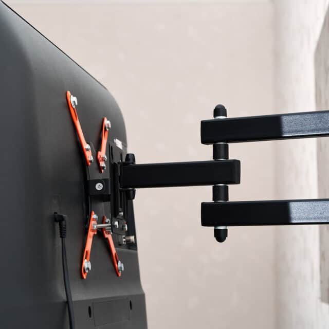 Back view of a wall-mounted flat-screen TV with an adjustable black and orange bracket.