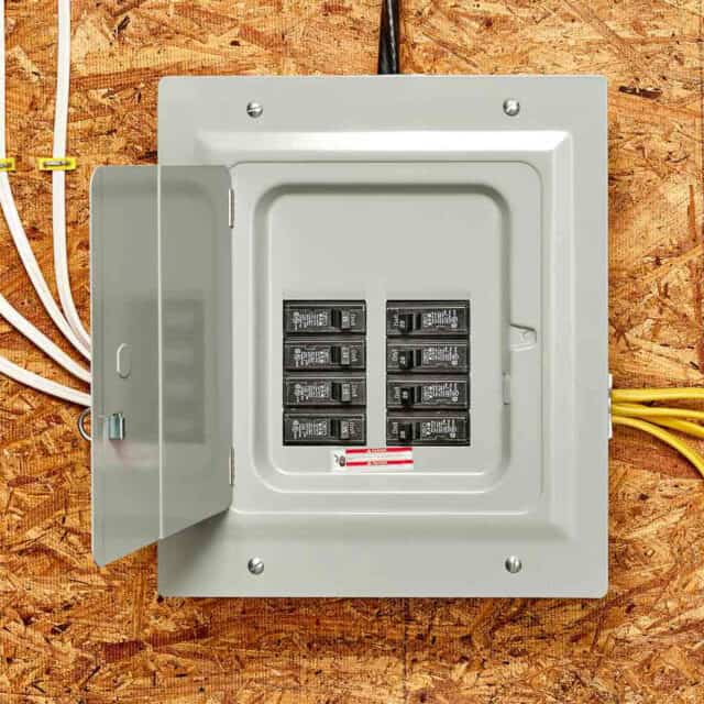 An open electrical panel with circuit breakers mounted on a plywood wall, showing wires entering from the top and right side.